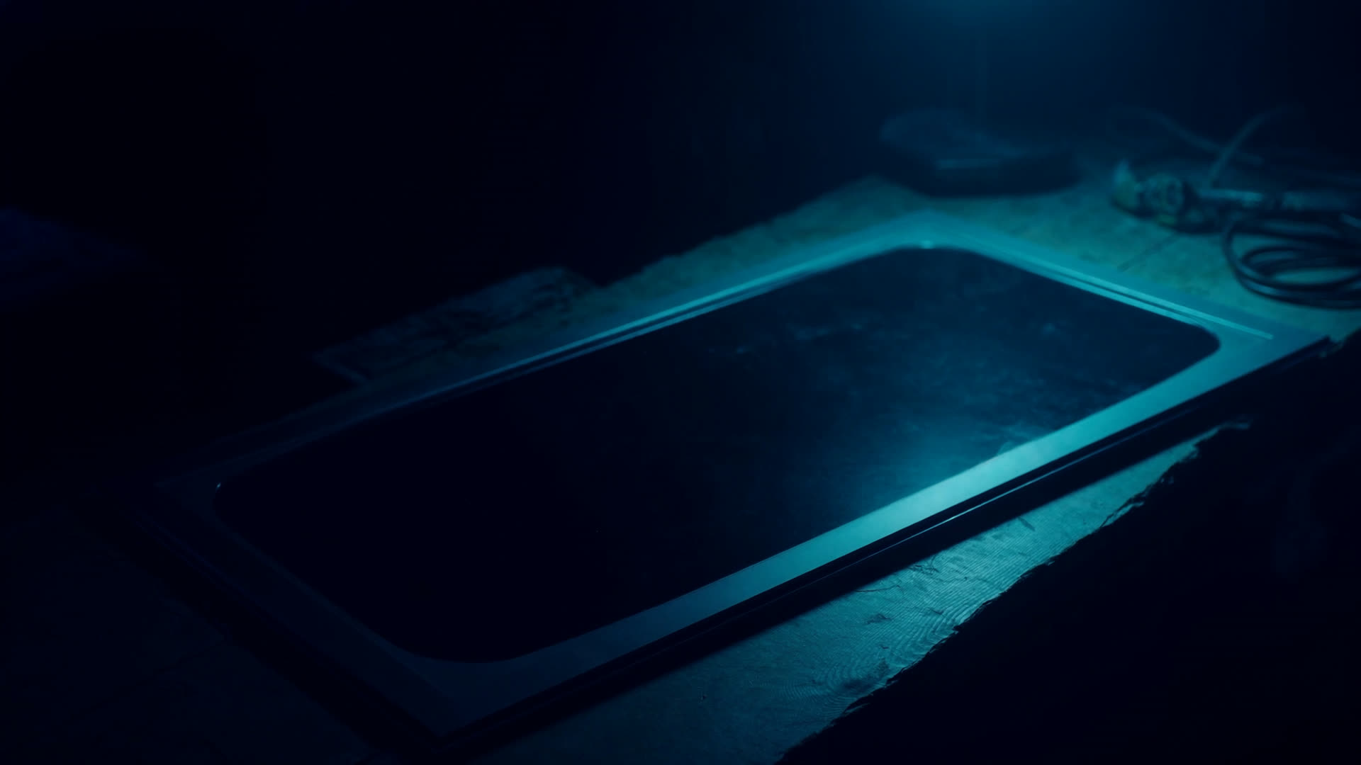 A PRISM glass panel lying on the workbench in the ReconIX lab under a single teal task lamp.